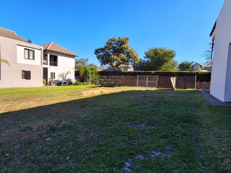 A spacious rear garden area featuring a lawn, timber boundary fencing, and a paved patio section adjacent to the residential building.