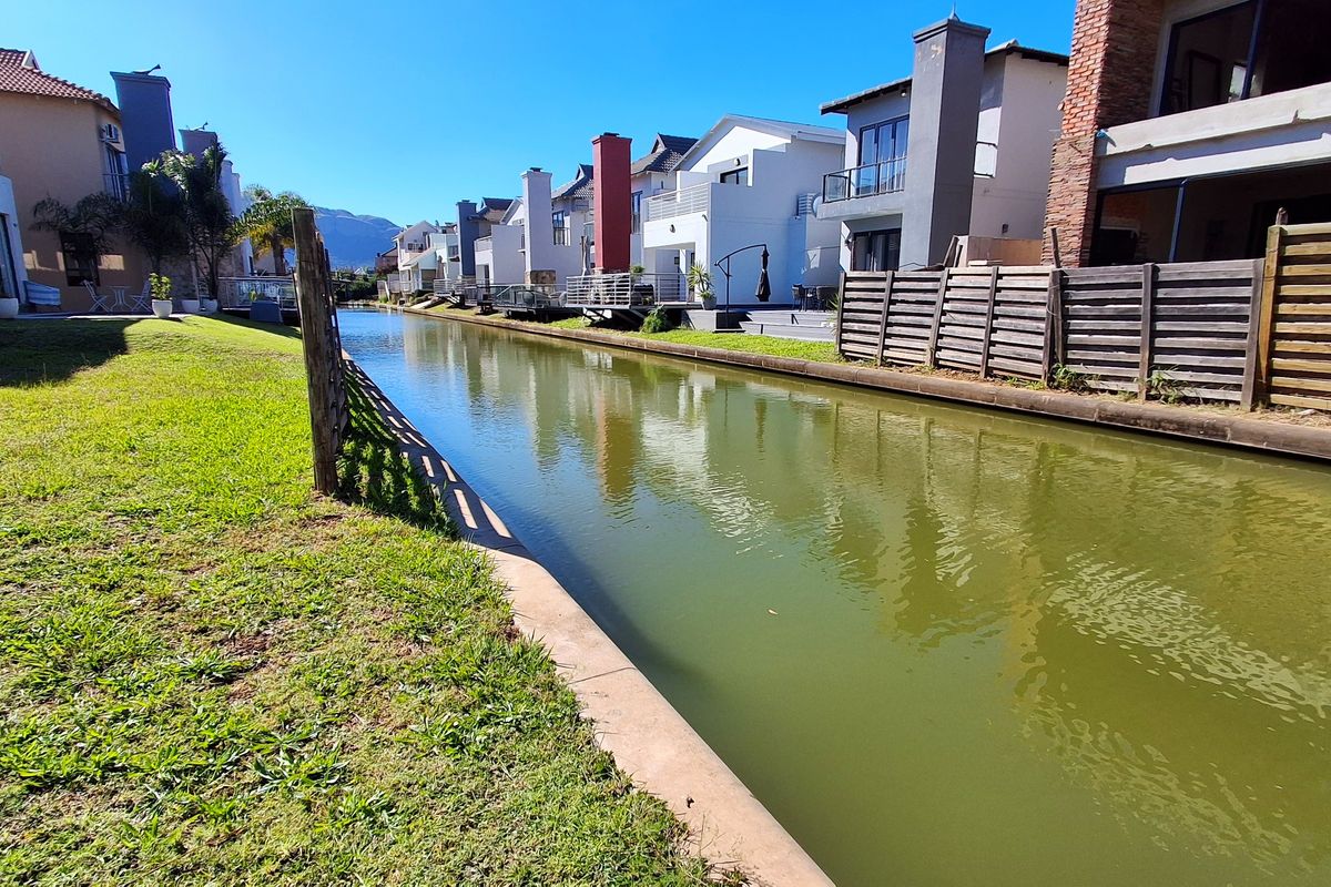 A view of the rear exterior of the residential properties featuring a canal, manicured lawn, and timber boundary fencing.