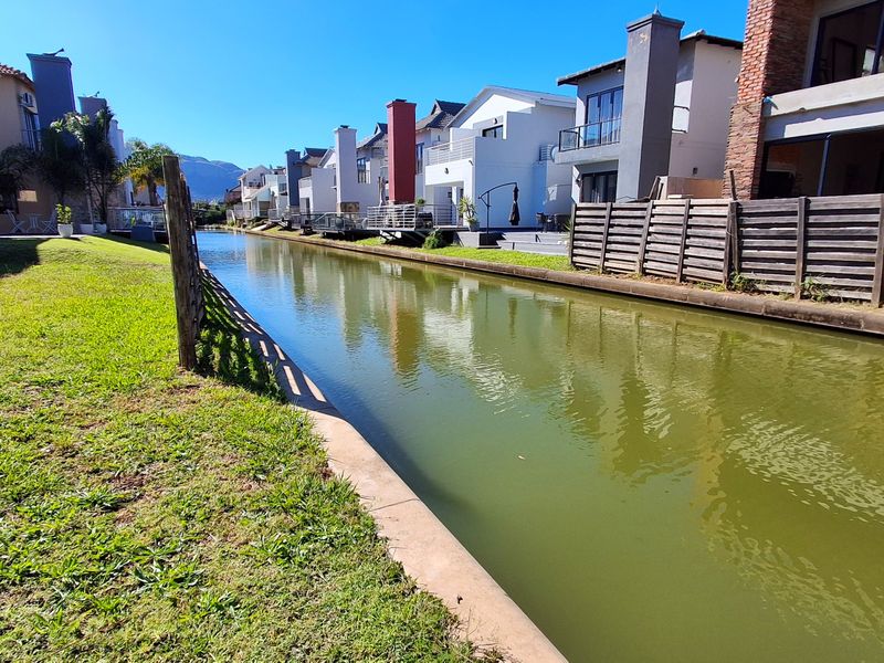 A view of the rear exterior of the residential properties featuring a canal, manicured lawn, and timber boundary fencing.