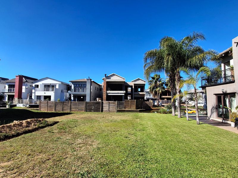 A well-maintained rear garden area featuring a manicured lawn, mature palm trees, and timber fencing, overlooking a residential canal setting.