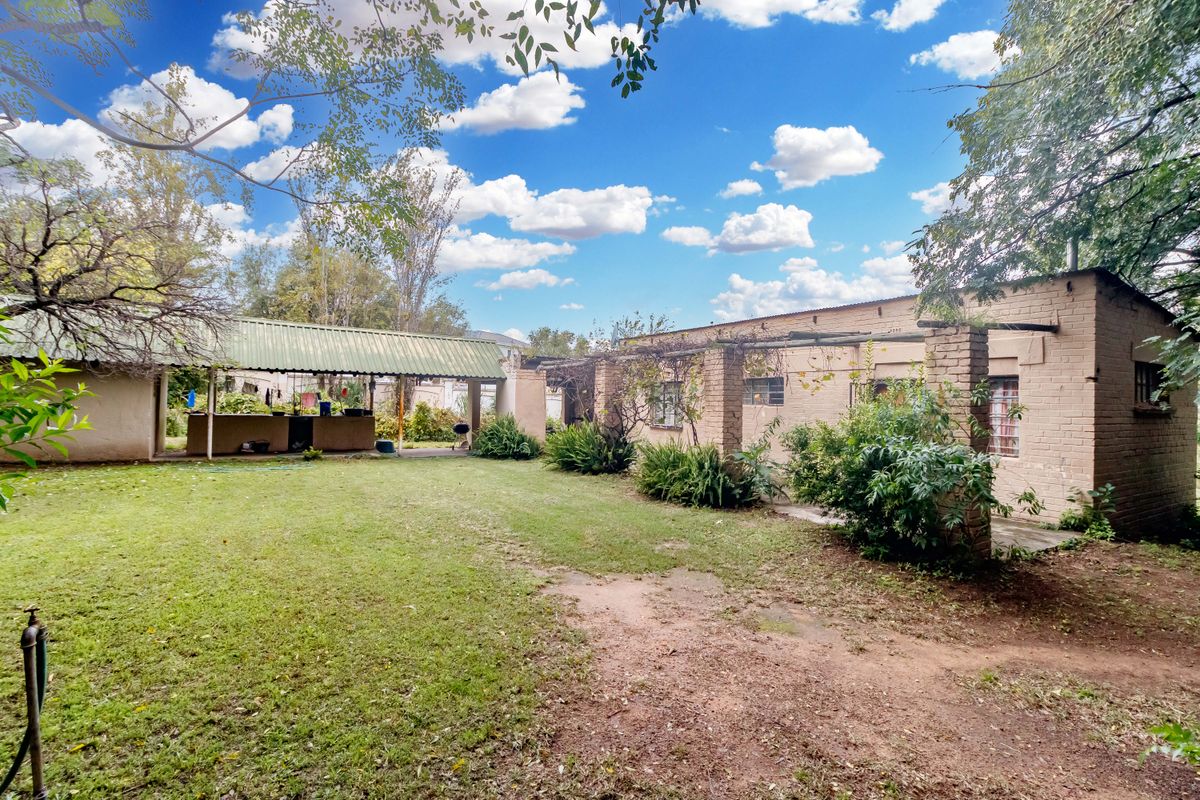 Rear view of the property featuring a brick facade, a covered patio area, and a spacious lawn with established garden beds.