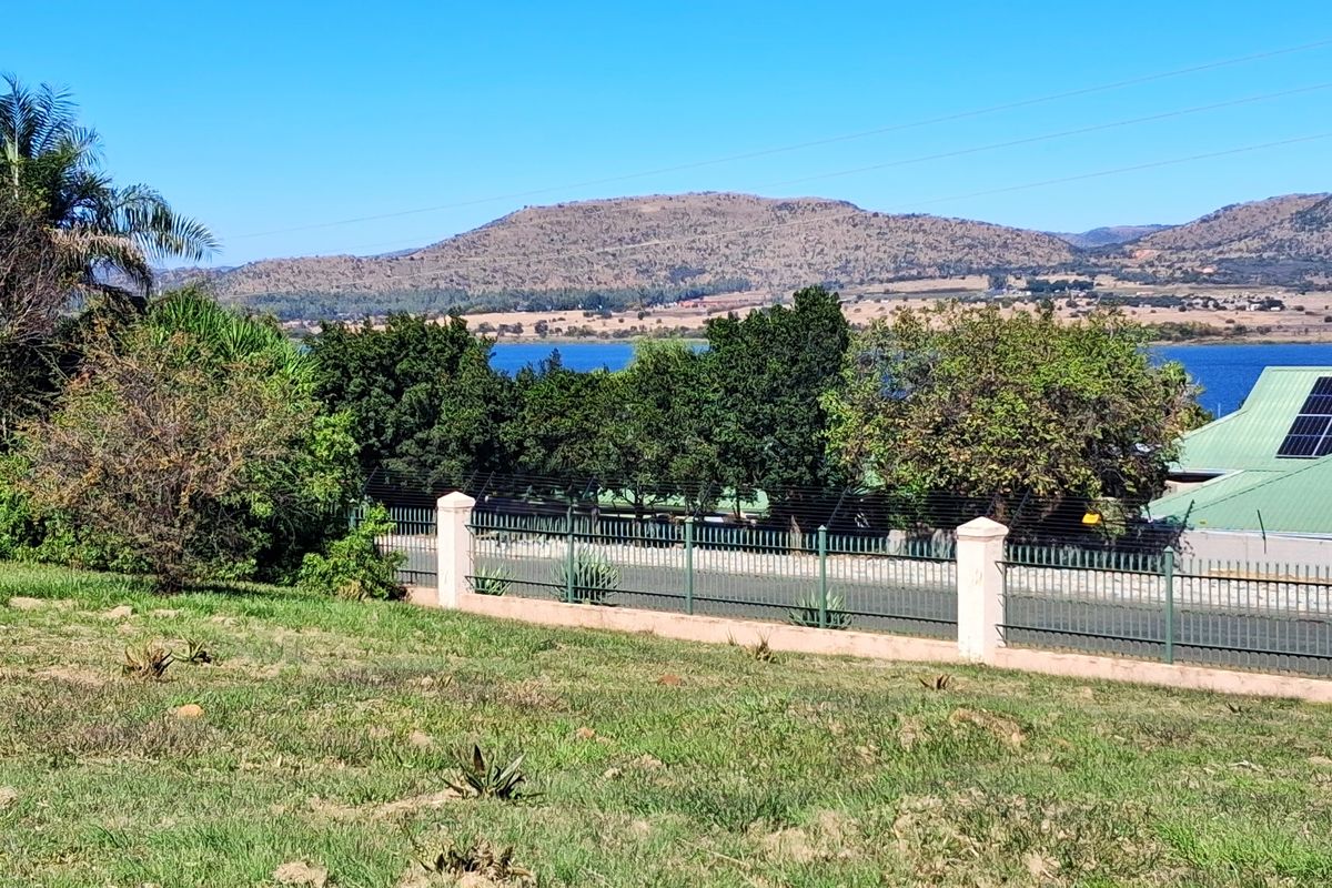 A scenic view of the surrounding landscape, lake, and mountains, featuring a fenced boundary and a nearby building with solar panels.