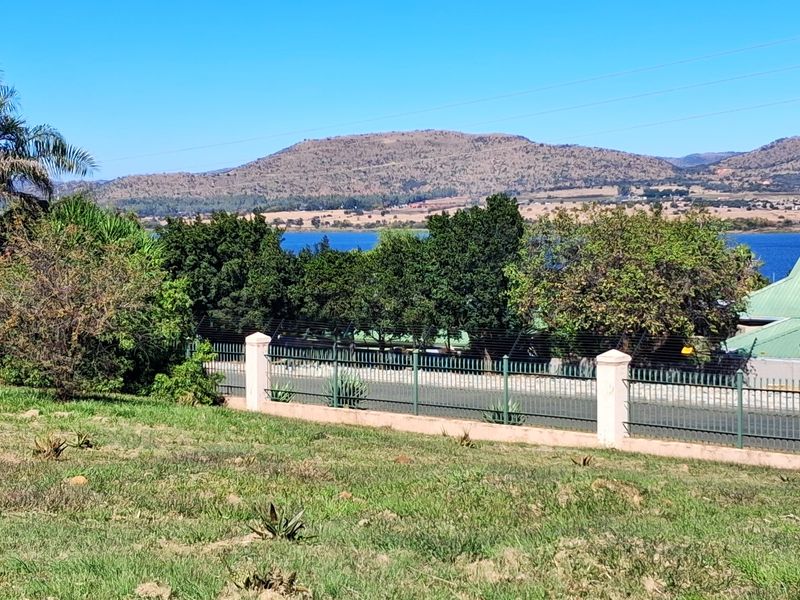 A scenic view of the surrounding landscape, lake, and mountains, featuring a fenced boundary and a nearby building with solar panels.