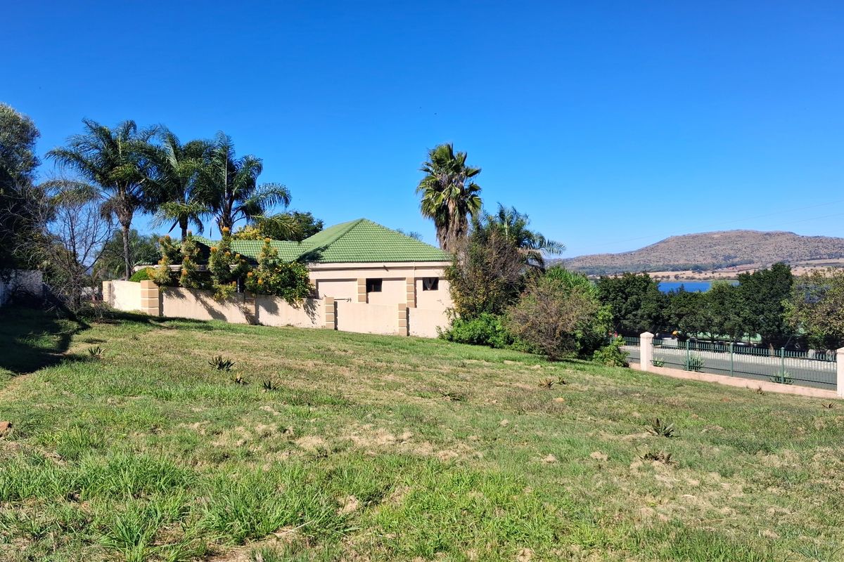 A view of a residential vacant land plot featuring a perimeter wall, established trees, and a view of the surrounding landscape and water.
