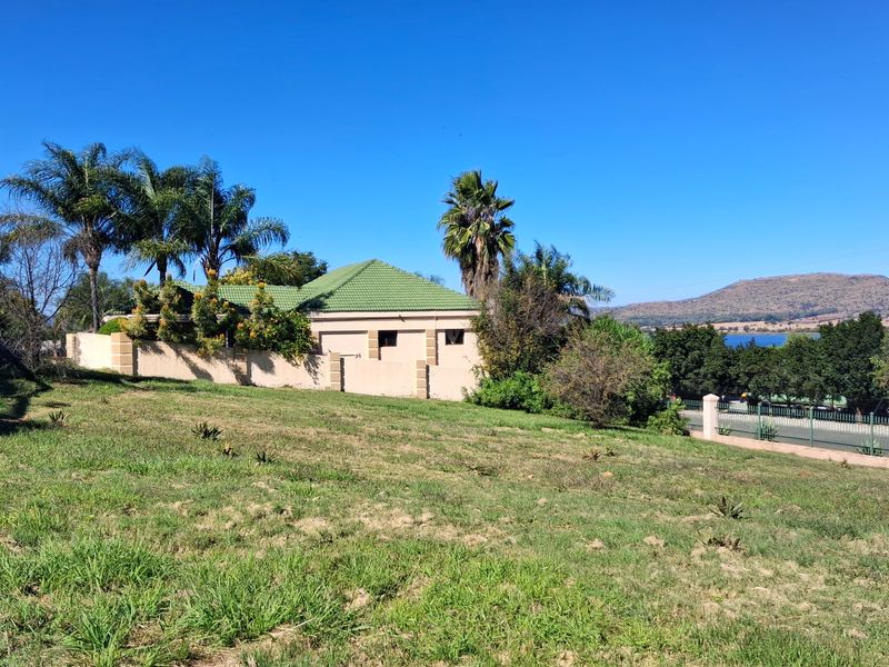 A view of a residential vacant land plot featuring a perimeter wall, established trees, and a view of the surrounding landscape and water.