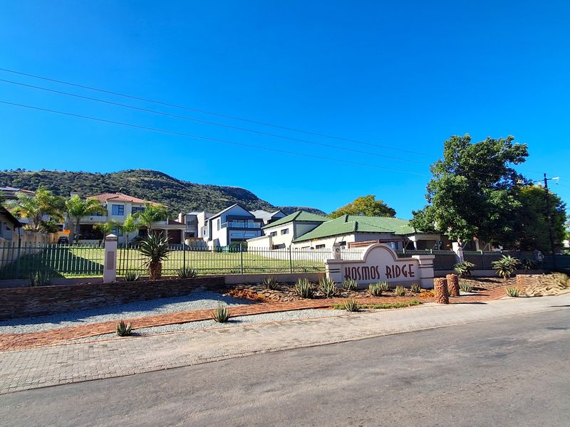 Street view of the Kosmos Ridge estate entrance, featuring clear signage, perimeter fencing, and well-maintained landscaping.