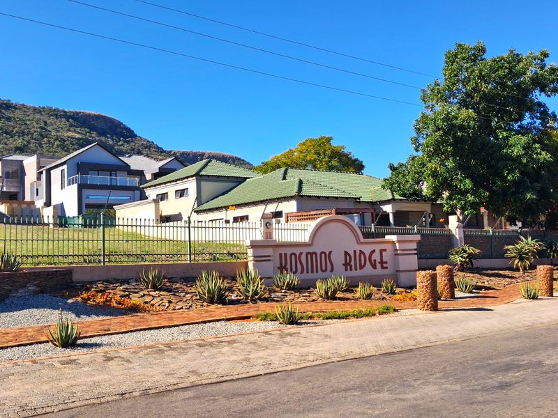 Street view of the Kosmos Ridge estate entrance featuring established landscaping, perimeter fencing, and clear signage.