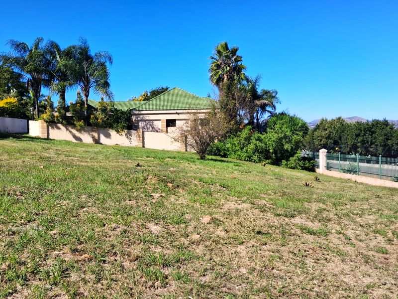 A view of a residential vacant land plot featuring a perimeter wall, metal fencing, and established garden greenery.