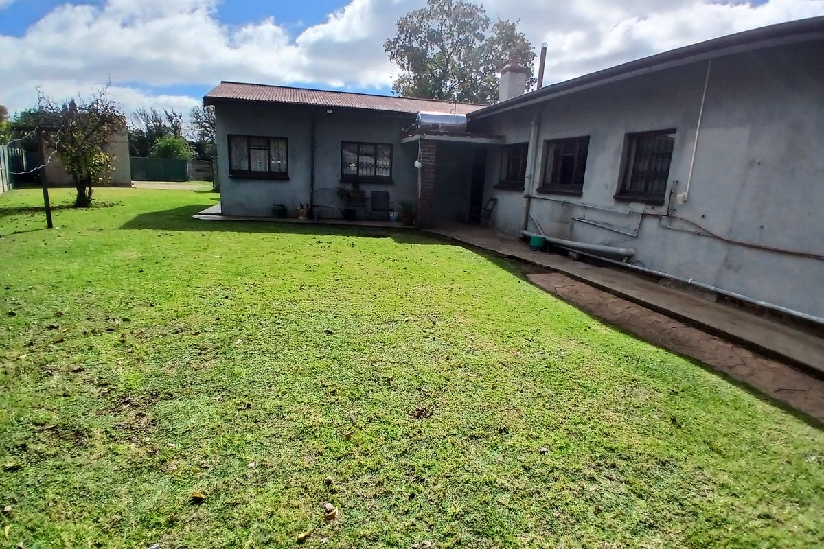 Rear view of the property featuring a large lawn, concrete pathway, and exterior wall with solar water heating system.