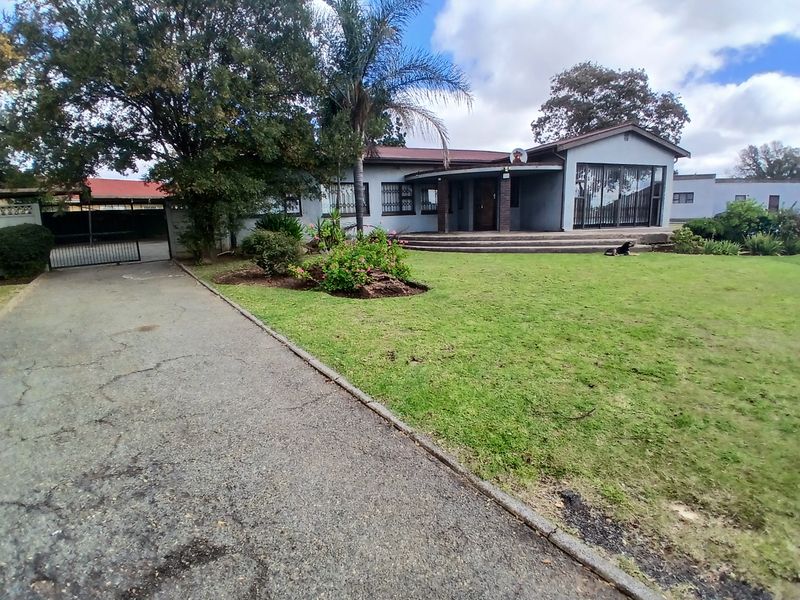 Front exterior view of a single-story house featuring a large lawn, asphalt driveway, security gate, and covered porch entrance.