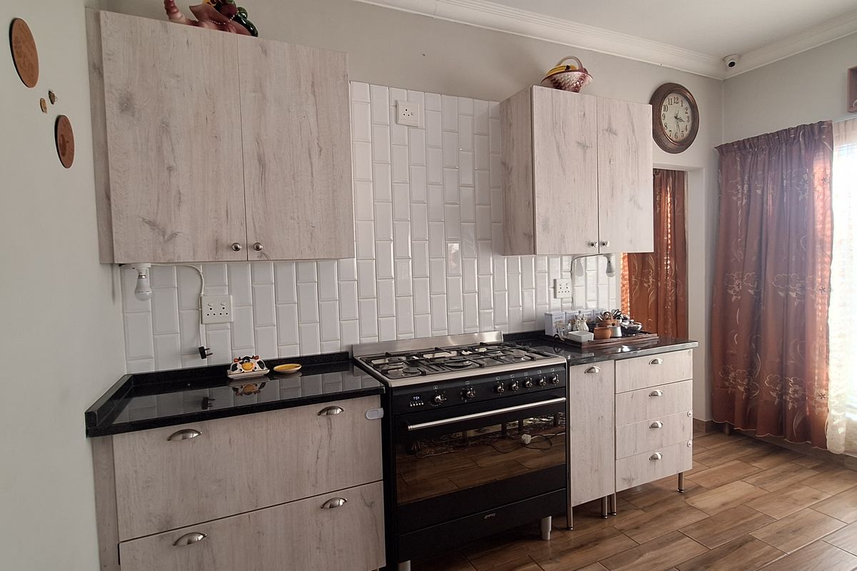 A modern kitchen featuring light wood-grain cabinetry, black granite countertops, a gas stove with oven, and a white subway tile backsplash.