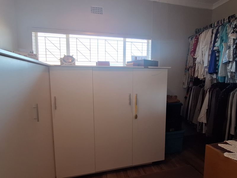 Bedroom featuring built-in cupboards, laminate flooring, and a window with security bars.