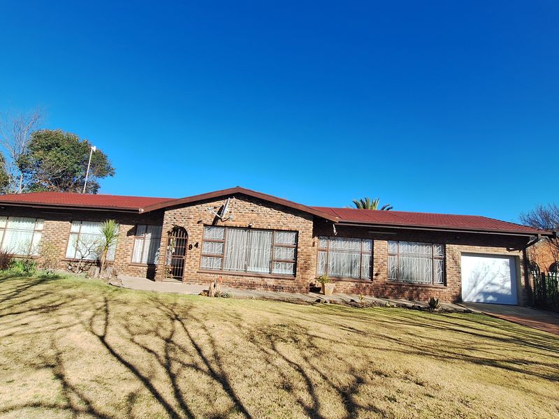 A single-story brick house with a metal roof, featuring a front lawn, large windows, and an integrated single garage.