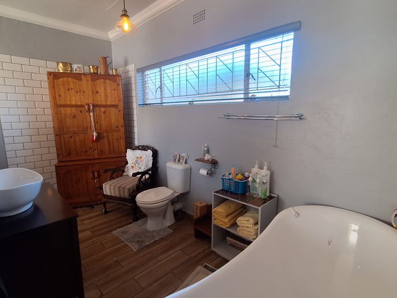 A well-lit bathroom featuring a freestanding bathtub, vessel sink, subway tile accents, and wood-look flooring, offering a functional and classic aesthetic.