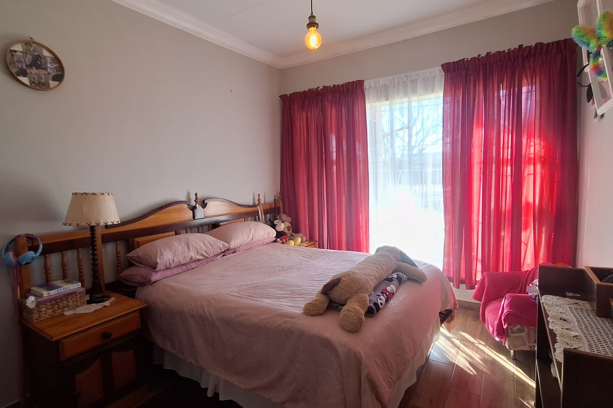 A cozy bedroom featuring wood-look tile flooring, cove cornicing, and a central pendant light fixture, offering a comfortable and functional living space.