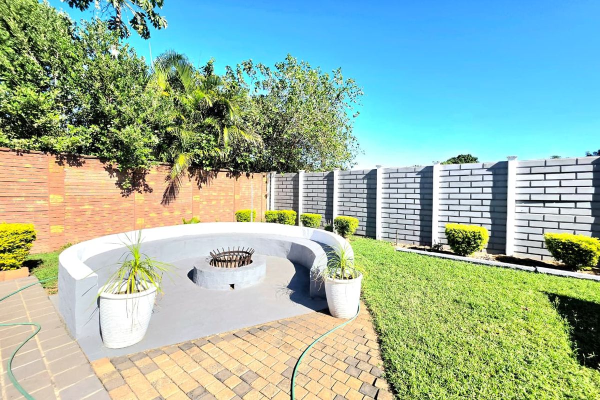 A well-maintained rear garden featuring a paved patio area with a built-in fire pit and curved concrete seating, enclosed by brick boundary walls.