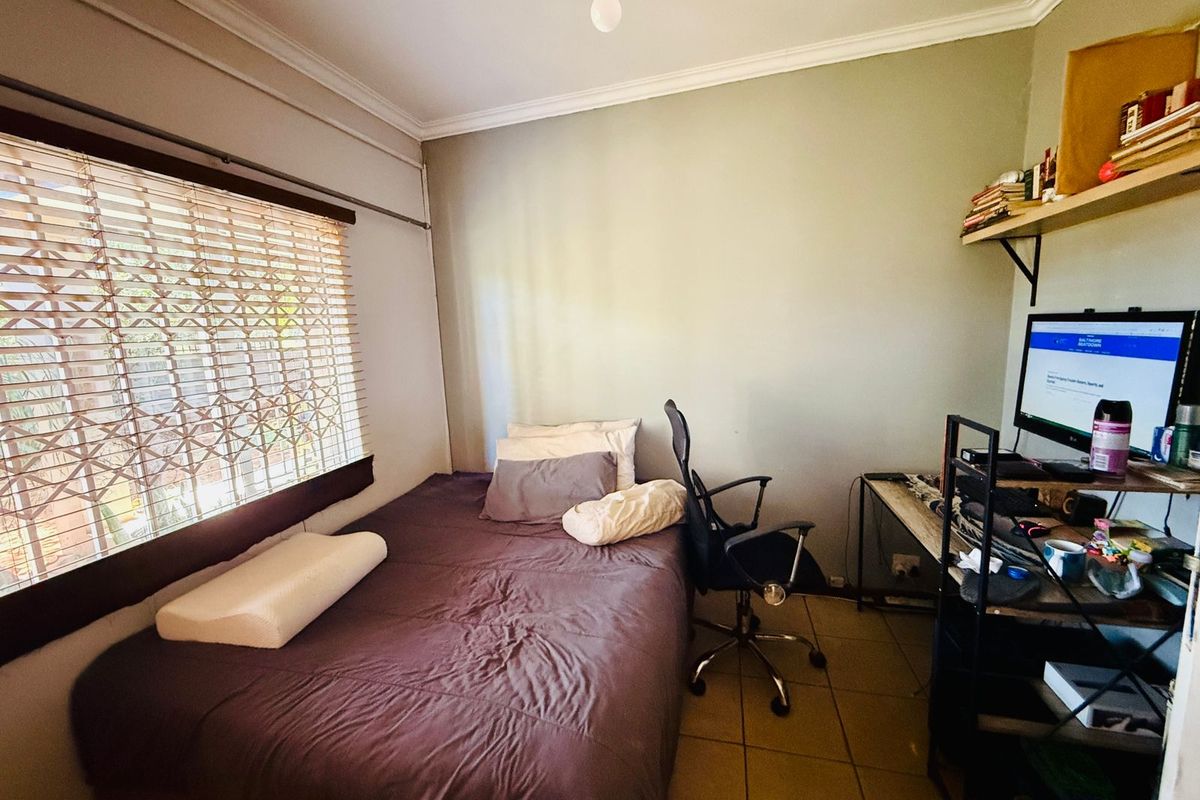 A functional bedroom featuring tiled flooring, a large window with security shutters, and crown molding.