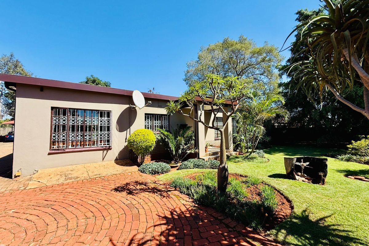 A view of the rear exterior of the house featuring a brick-paved patio area, landscaped garden, and established trees.