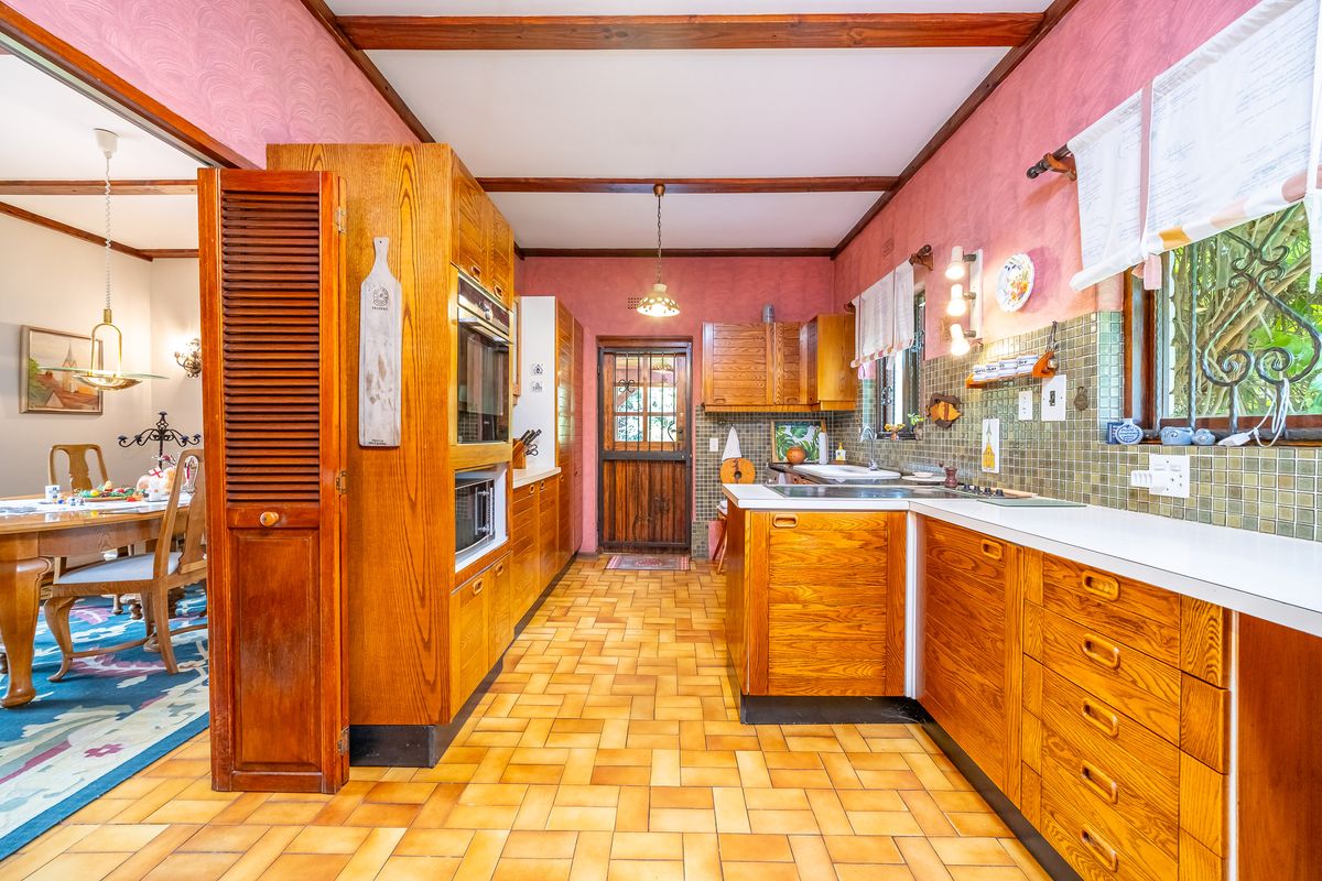 A traditional kitchen featuring extensive wooden cabinetry, tiled flooring, exposed ceiling beams, and a functional layout with built-in appliances.