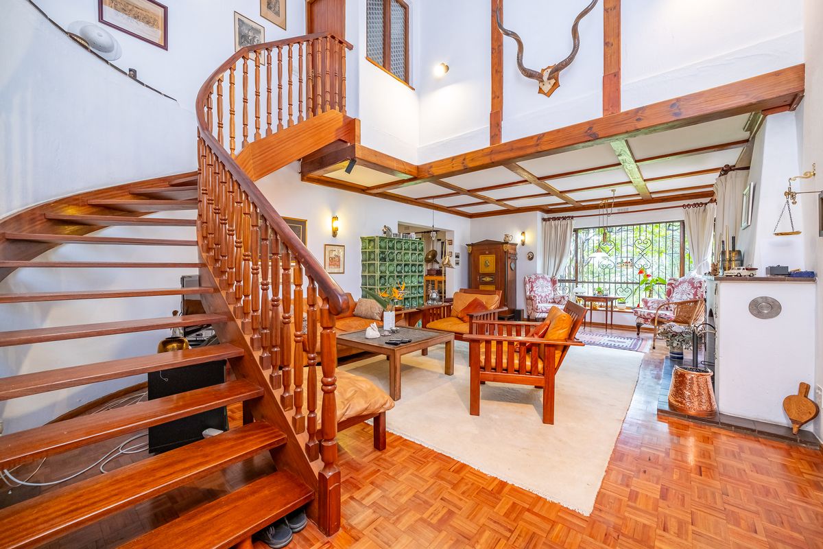 Spacious living room featuring a prominent wooden spiral staircase, exposed timber ceiling beams, parquet flooring, and a traditional fireplace with a tiled stove.