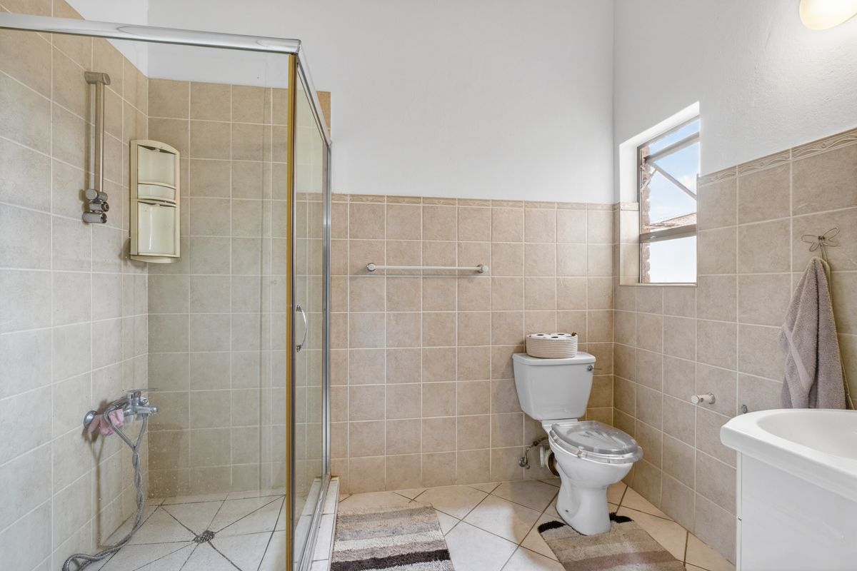 A functional bathroom featuring a glass shower enclosure, tiled walls and flooring, a standard toilet, and a vanity basin.
