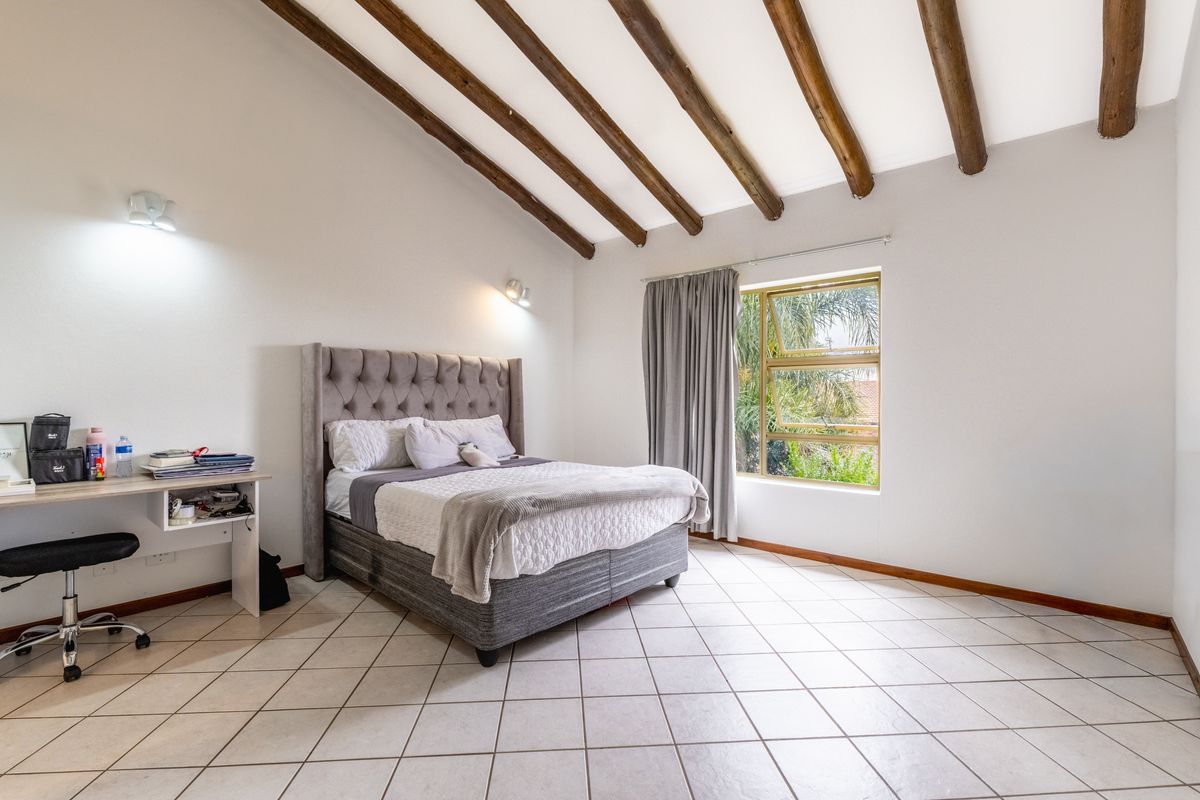 Spacious bedroom featuring exposed timber ceiling beams, tiled flooring, and natural light through a large window.