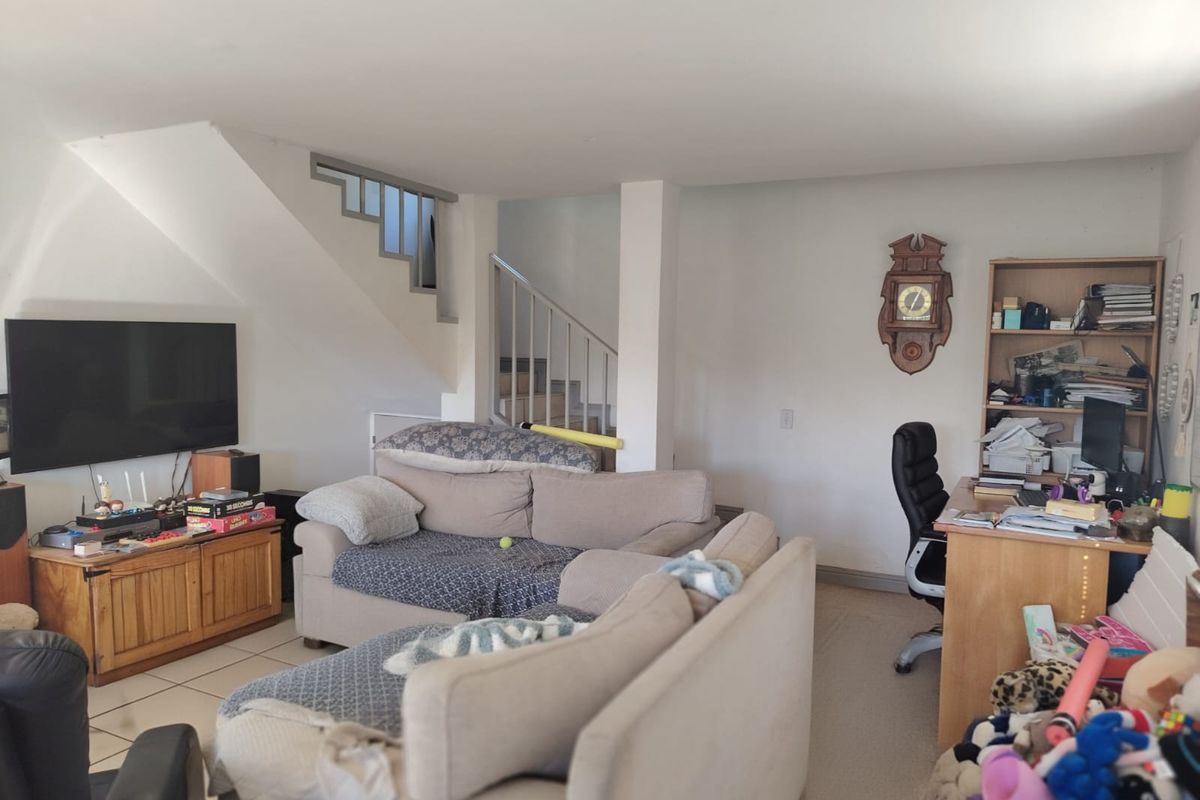 A living room area featuring a staircase, tiled and carpeted flooring, and an open-plan layout suitable for versatile furniture arrangements.