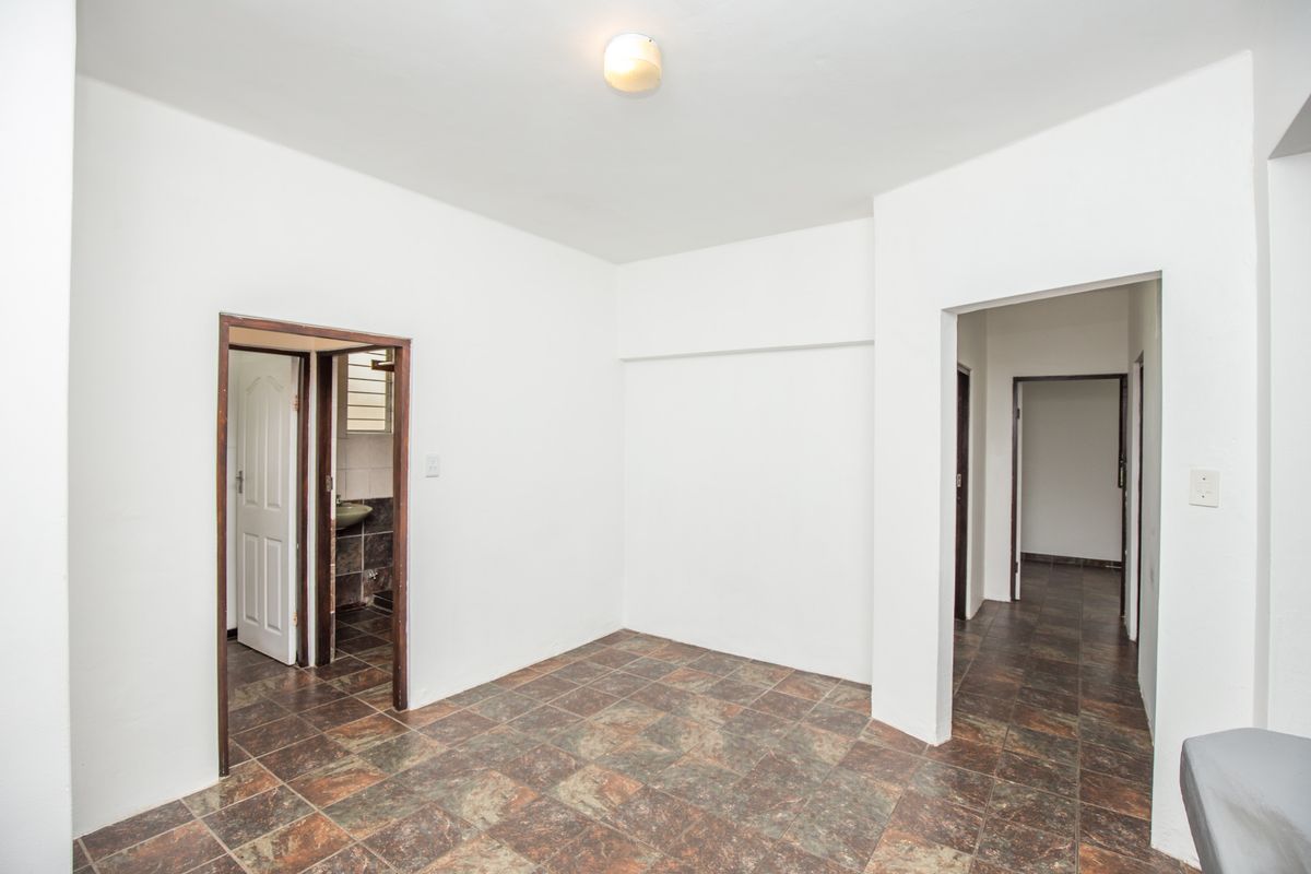An empty interior space featuring tiled flooring, white walls, and access to adjacent rooms, including a bathroom with tiled finishes.