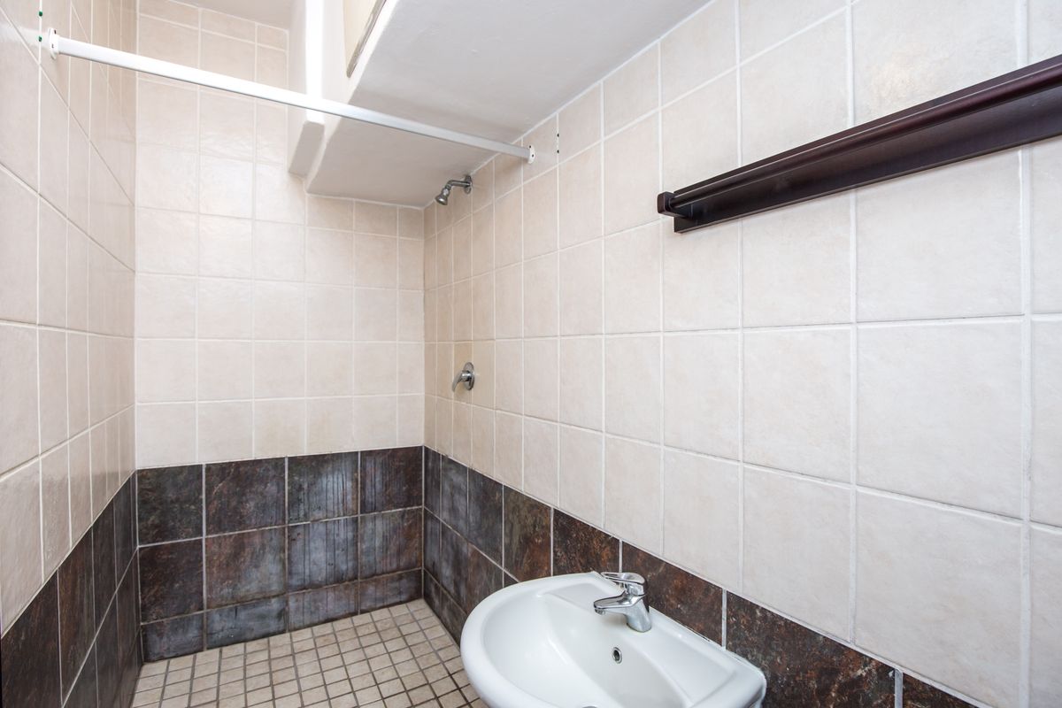 A functional bathroom featuring a wall-mounted basin, shower head, and two-tone tiled walls with a neutral color palette.