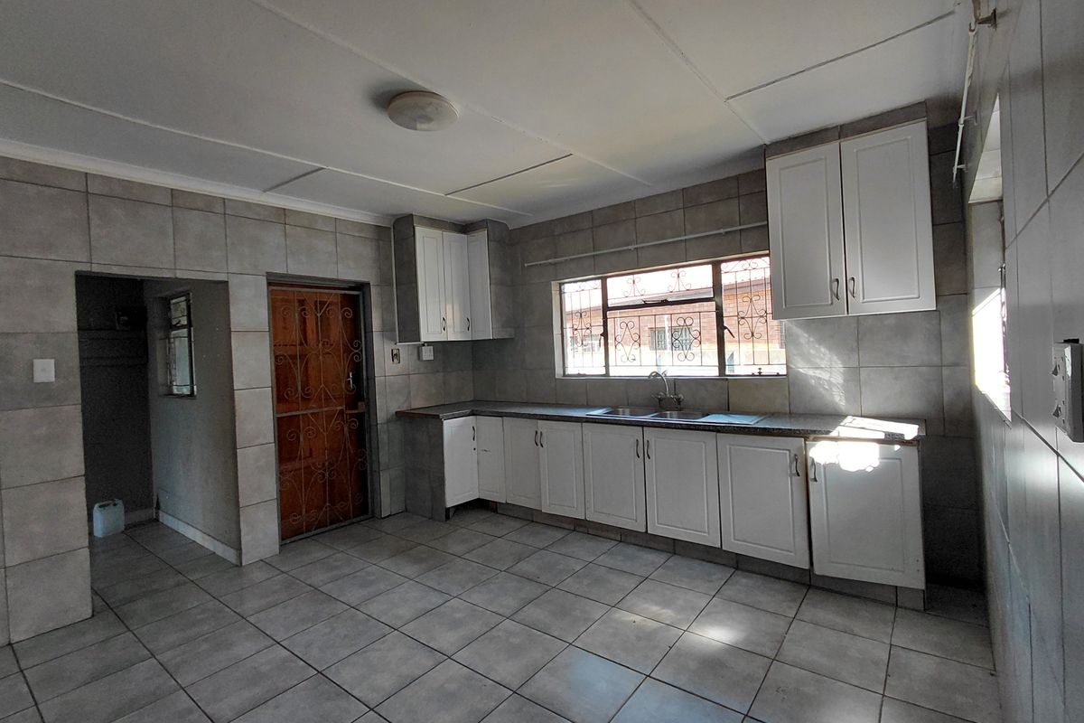 A spacious, empty kitchen featuring tiled walls and floors, white built-in cabinetry, and a double sink, ready for modernization.