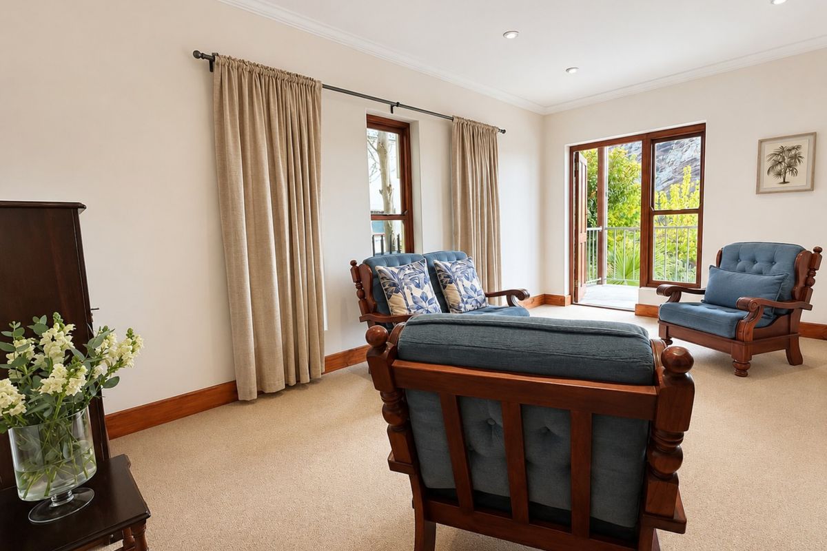 A bright living room featuring neutral carpet, recessed downlights, and timber-framed windows and doors leading to an outdoor balcony area.