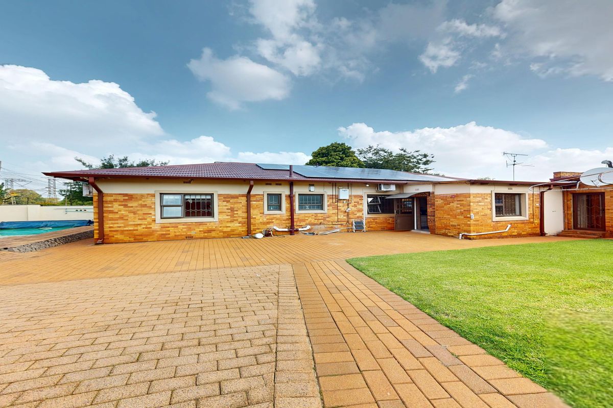 Rear view of a brick house featuring a paved patio, a swimming pool, and a well-maintained lawn with solar panels installed on the roof.
