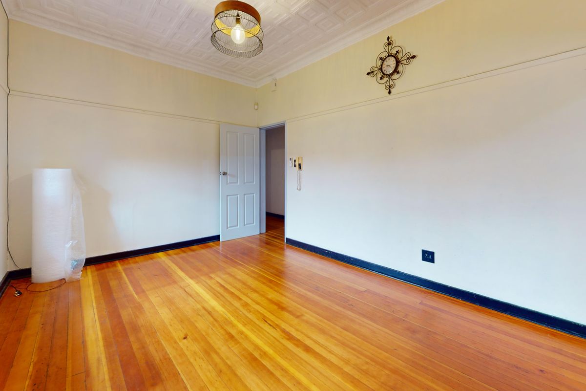 A bright, empty bedroom featuring polished timber flooring, a classic pressed metal ceiling, and security bars on the window.
