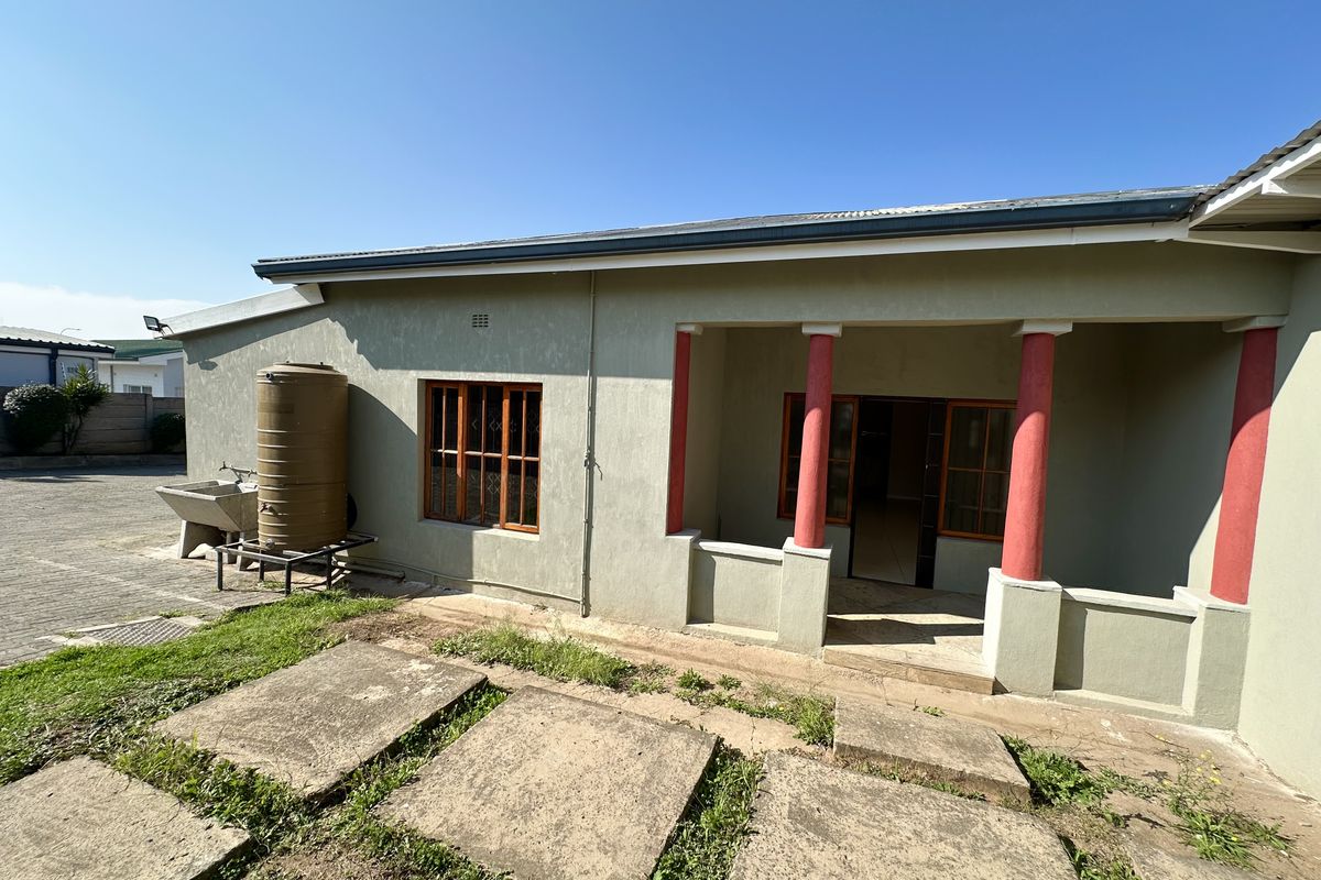 Rear exterior view of the house featuring a covered patio with decorative columns, a water storage tank, and a concrete wash basin area.