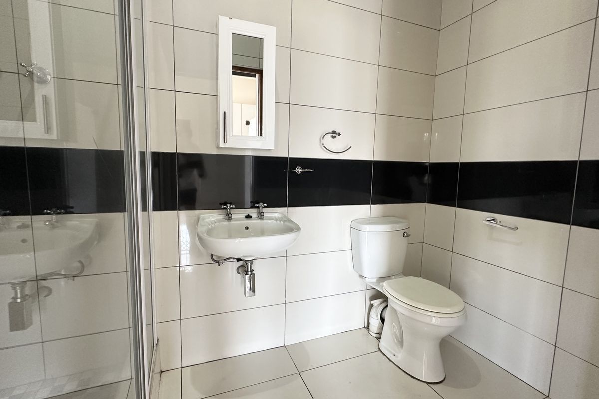 A clean, modern bathroom featuring a wall-mounted basin, toilet, and a glass-enclosed shower with contrasting black and white wall tiles.