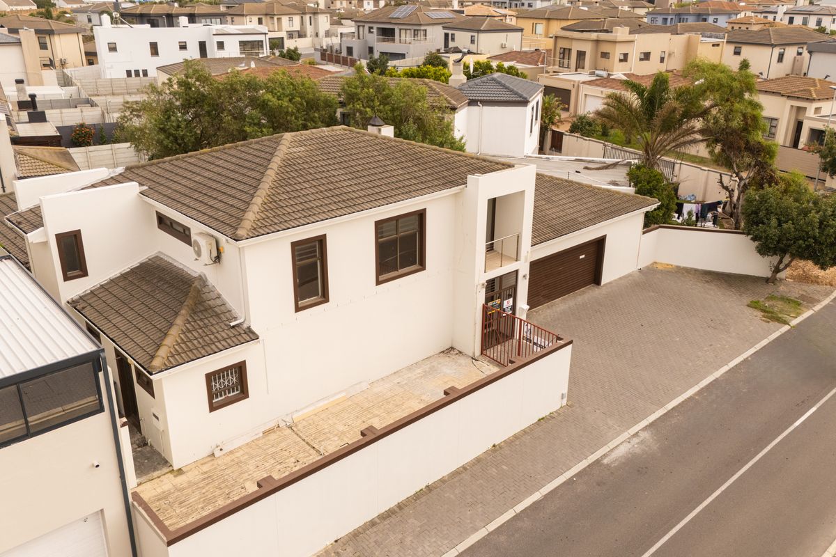 Aerial view of a residential property featuring a tiled roof, paved driveway, and secure boundary wall in a suburban estate setting.