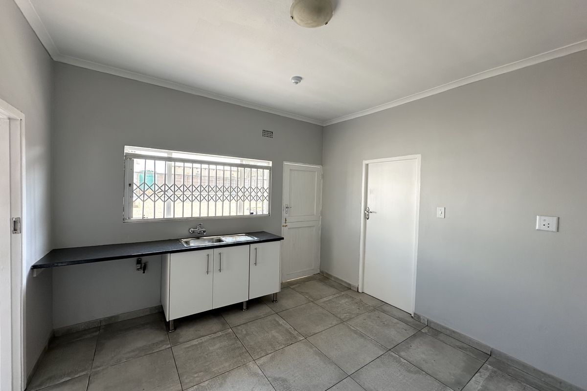 A functional, empty kitchen area featuring tiled flooring, base cabinetry with a stainless steel sink, and security bars on the window.