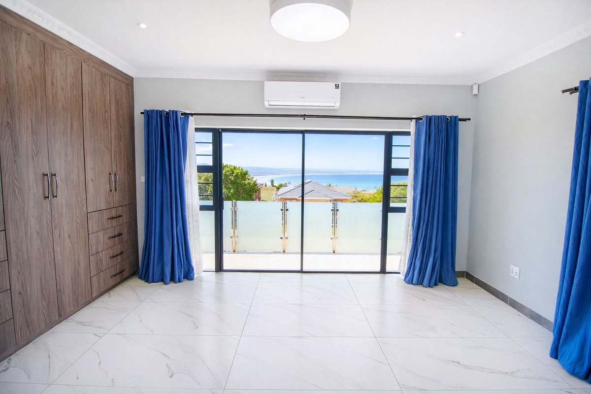 Spacious bedroom featuring built-in cupboards, tiled flooring, air conditioning, and a sliding door opening to a balcony with scenic ocean views.