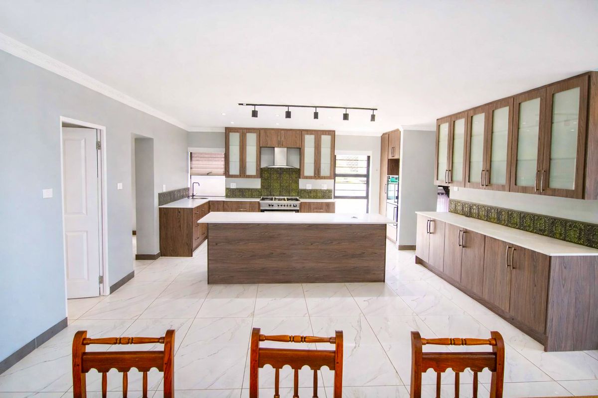 Spacious modern kitchen featuring wood-finish cabinetry, a central island, stone countertops, and integrated appliances with light-colored tiled flooring.