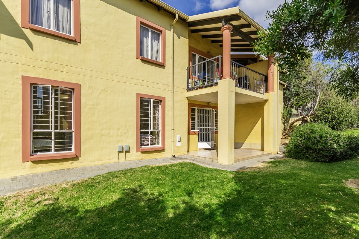 Rear view of the apartment building featuring a covered ground-floor patio, an upper-level balcony, and a well-maintained garden area.