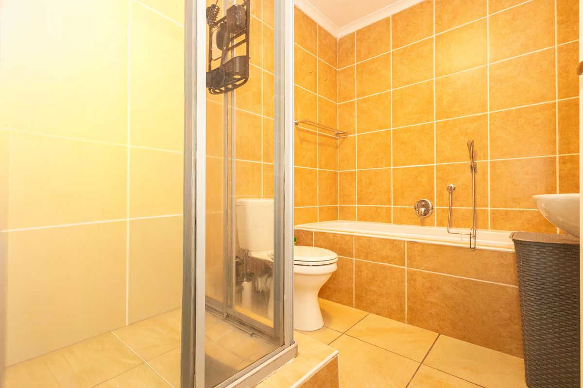 A functional bathroom featuring a shower enclosure, bathtub, toilet, and wall-mounted basin with warm-toned wall and floor tiling.