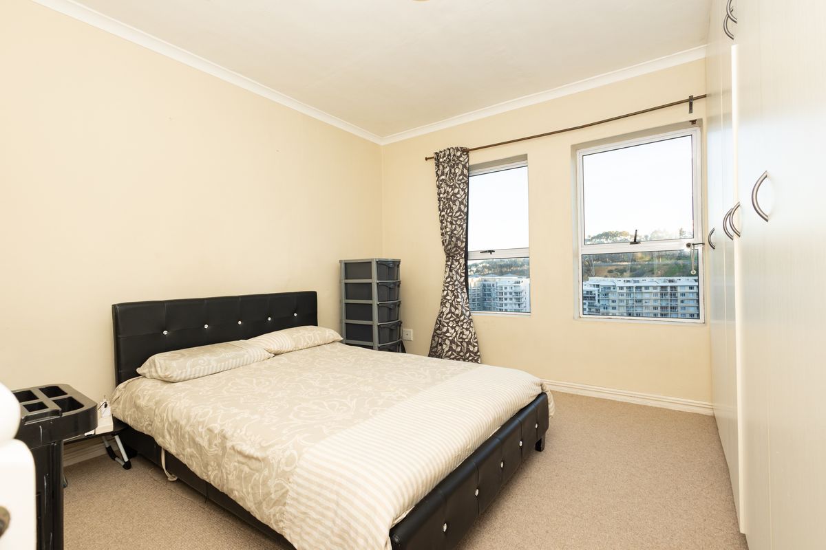 A well-lit bedroom featuring neutral walls, carpeted flooring, and built-in cupboards, offering a comfortable space with views through two large windows.