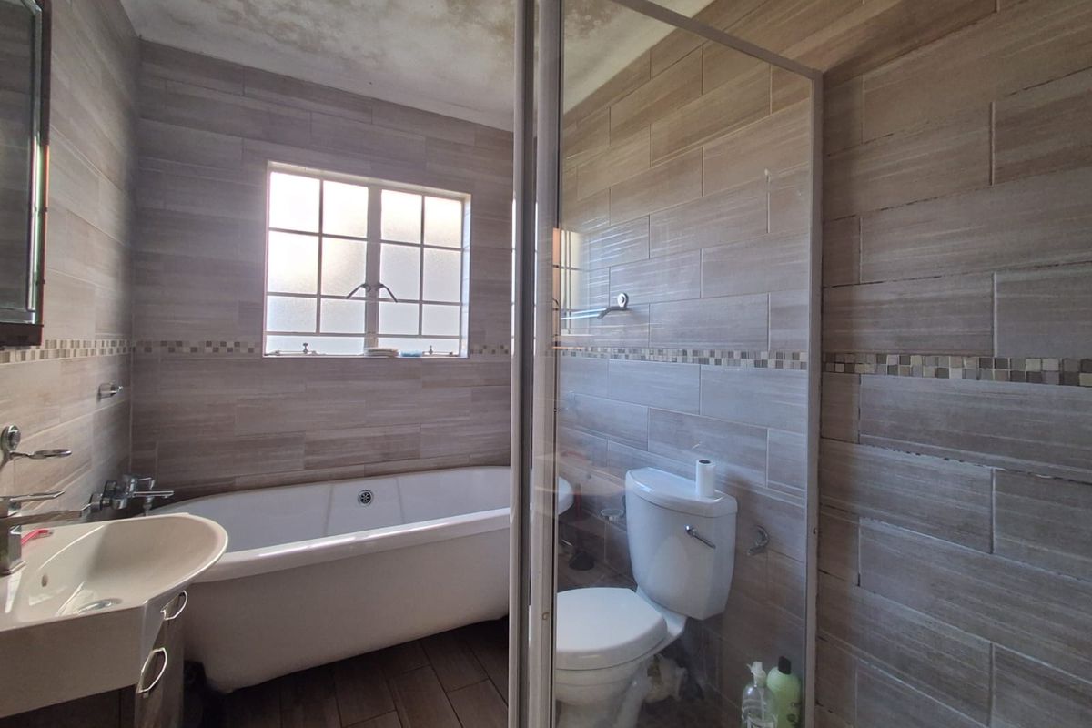 Bathroom featuring a freestanding bathtub, glass shower enclosure, toilet, and vanity basin with tiled finishes. Ceiling shows signs of water damage.