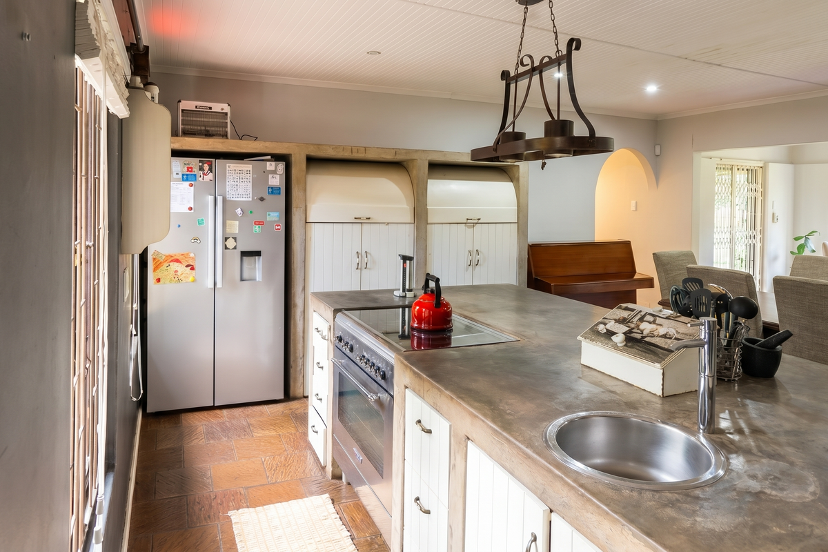 Spacious kitchen featuring a large concrete island with integrated cooktop and sink, complemented by custom cabinetry and a classic beadboard ceiling.