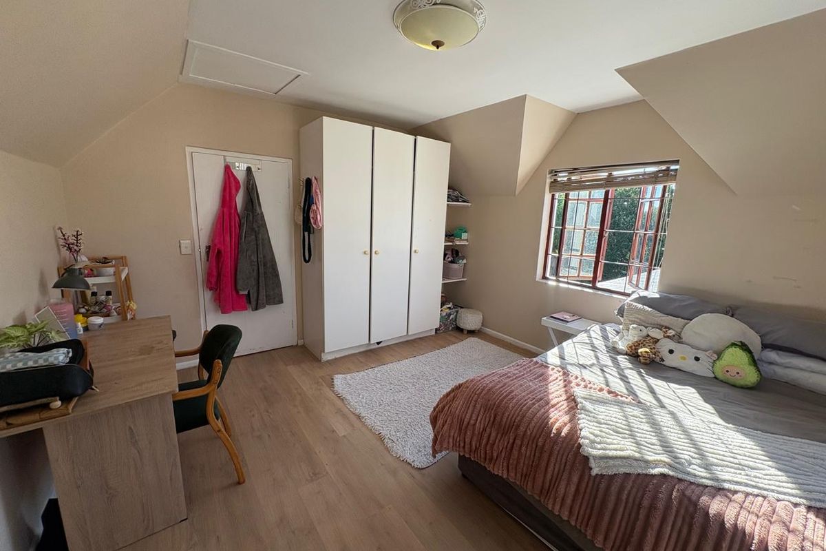 A cozy bedroom featuring built-in white cabinetry, laminate wood flooring, and a window with natural light, set under a sloped ceiling.