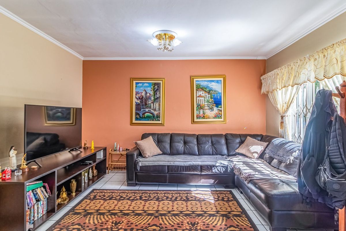 A comfortable living room featuring tiled flooring, crown molding, and a large window with security bars, providing a functional and well-lit space.