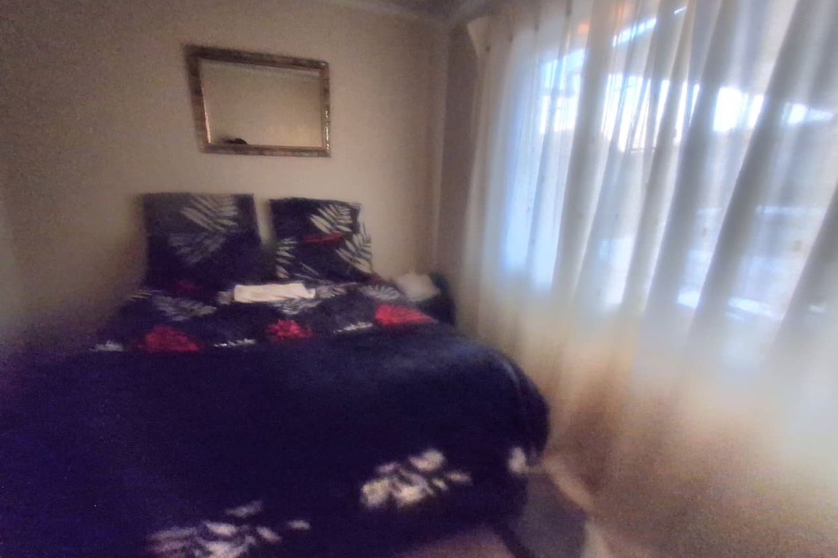 A bedroom featuring a window with sheer curtains and a wall-mounted mirror.