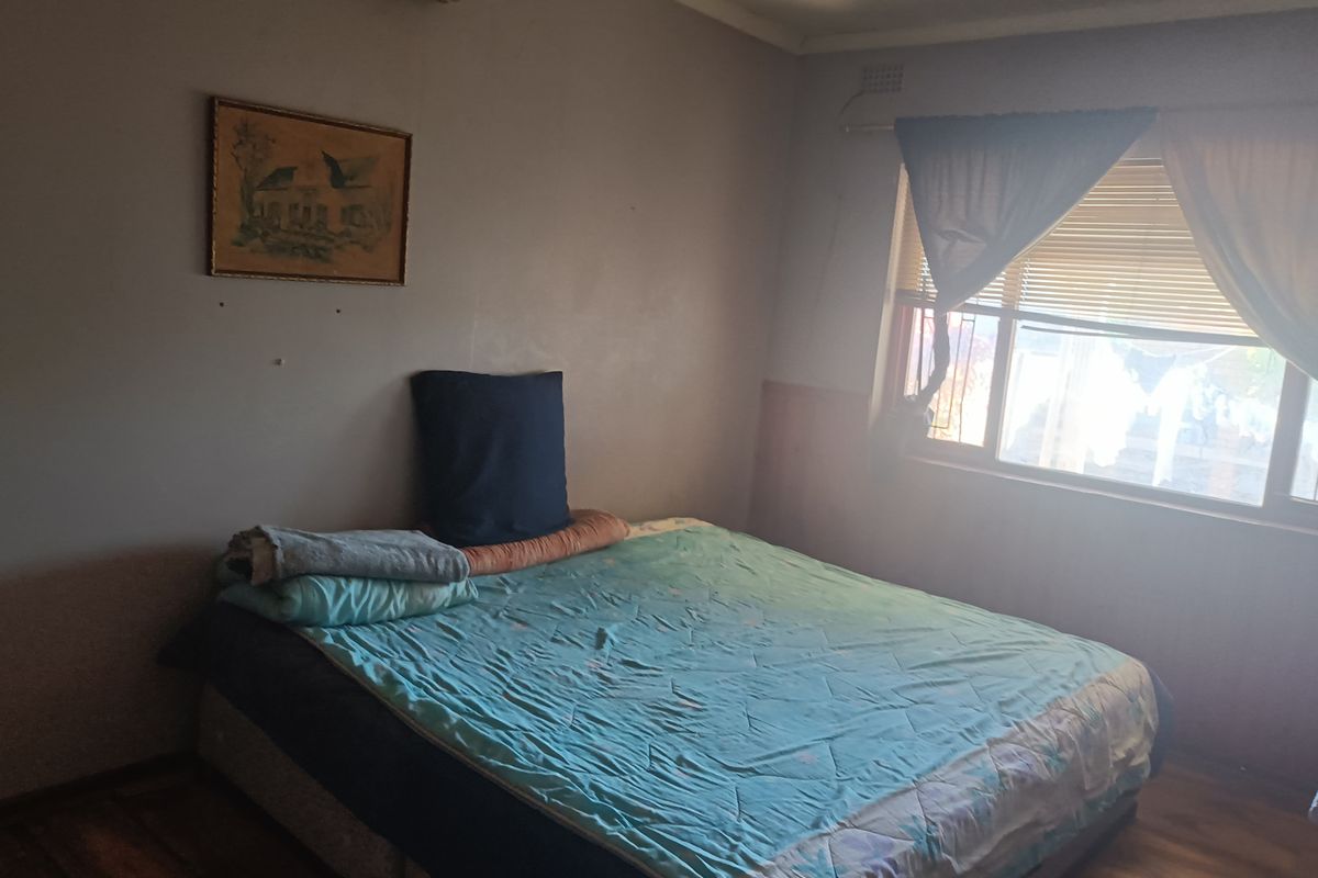 A bedroom featuring laminate flooring, an air conditioning unit, and a window with fitted blinds, requiring cosmetic updates to improve its overall appeal.