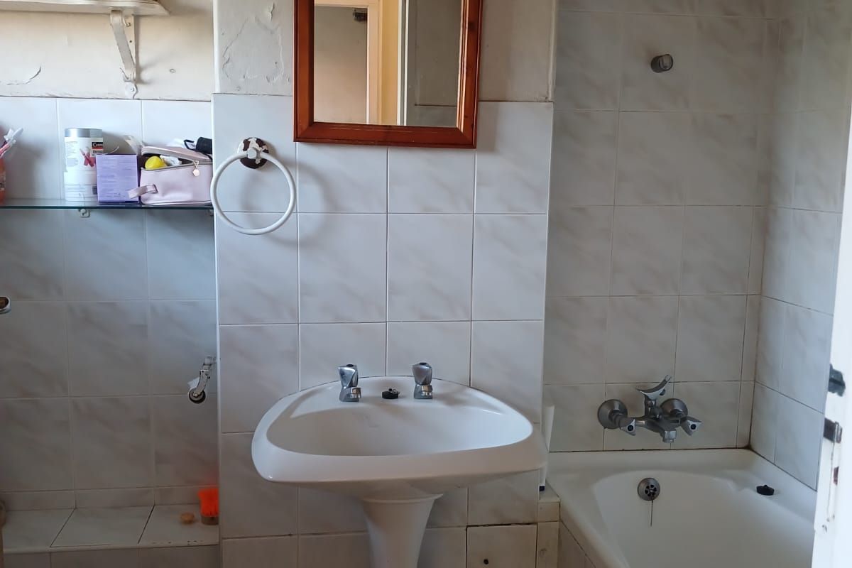 A dated bathroom featuring a pedestal basin, bathtub with shower mixer, and tiled finishes, currently requiring cosmetic renovation and maintenance.