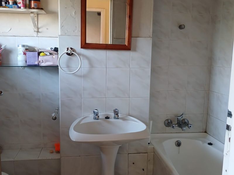 A dated bathroom featuring a pedestal basin, bathtub with shower mixer, and tiled finishes, currently requiring cosmetic renovation and maintenance.